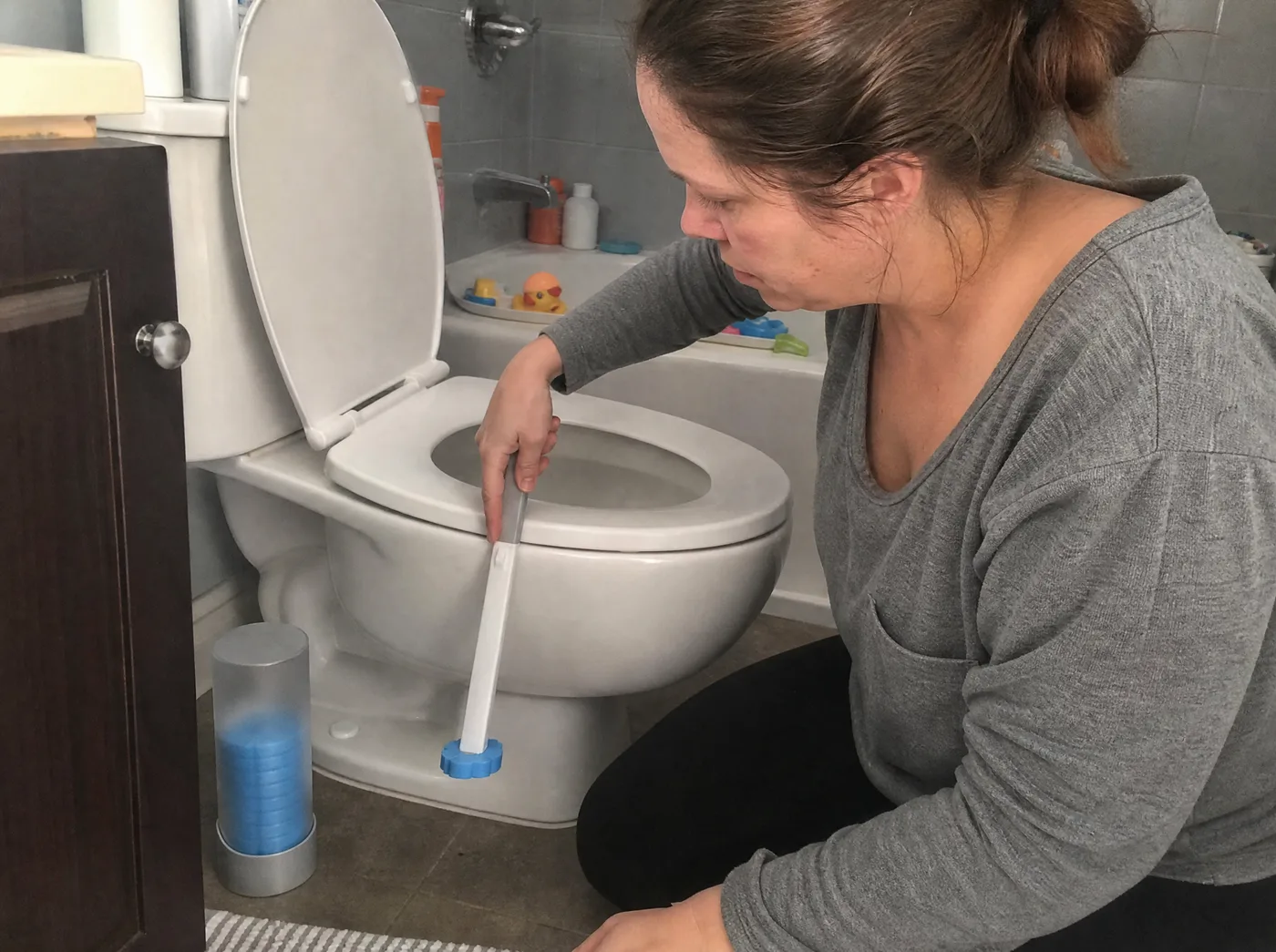 Mom cleaning a family toilet with the TossClean wand, refill caddy beside the toilet